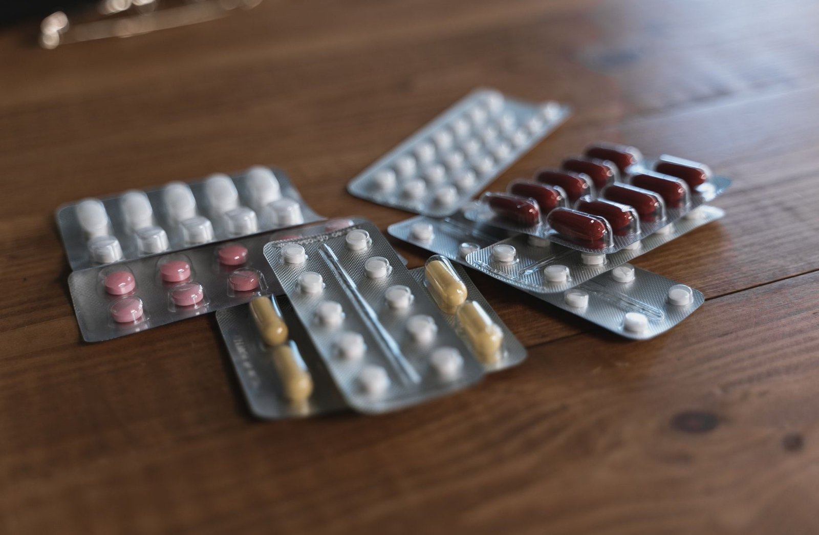 Several part-used blister packs of tablets and capsules spread across a wooden table