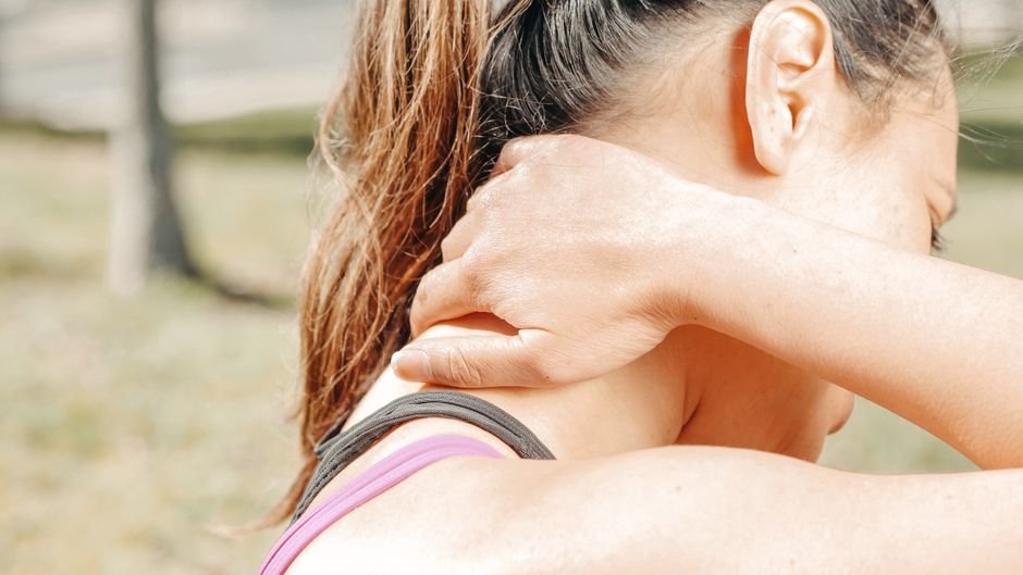 A person seated with one hand pressed to the back of the neck at the base of the skull