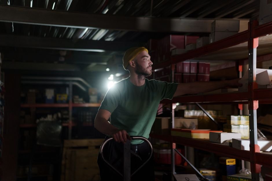 A worker in a high-visibility vest inside a large warehouse at night