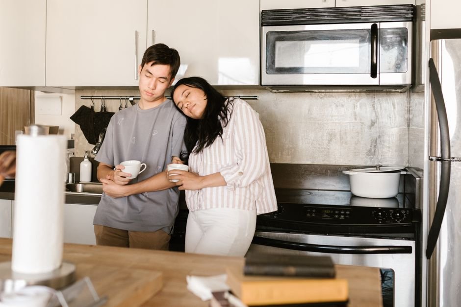 A woman standing in a kitchen in the morning with one hand to her forehead