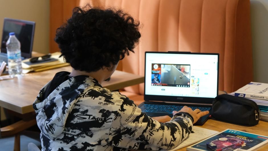 A teenager working at a laptop late at night in a dimly lit room