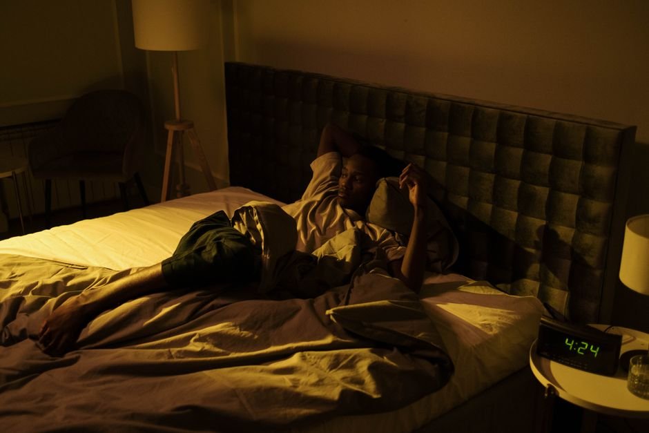 A person lying awake in bed in the dark with one arm across the forehead