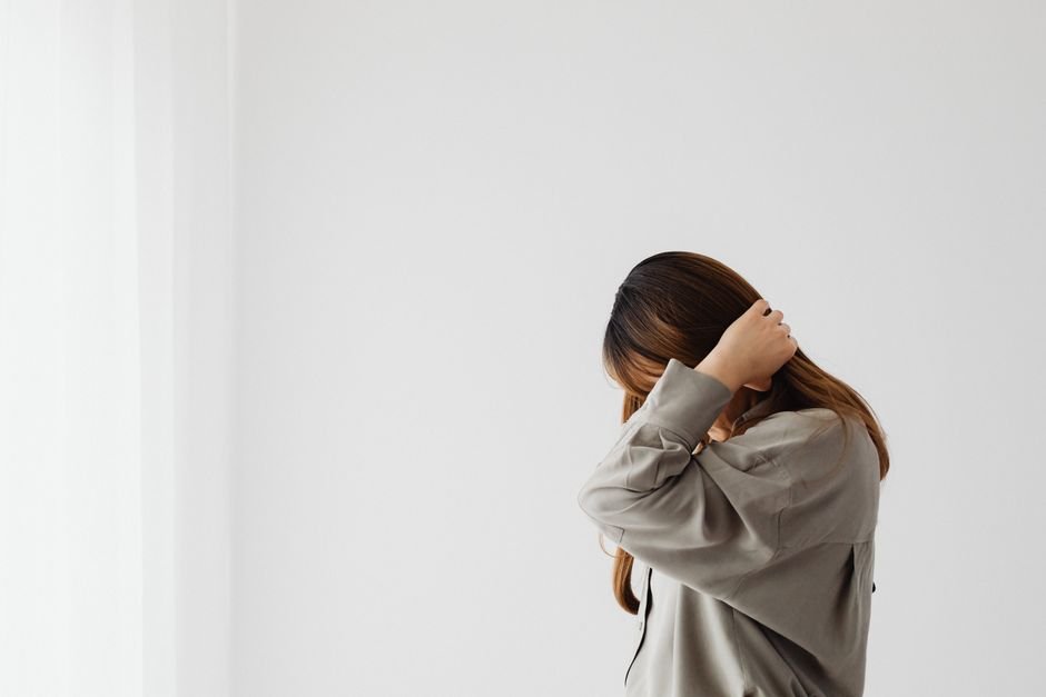 A woman standing with one hand against a wall and the other to her head