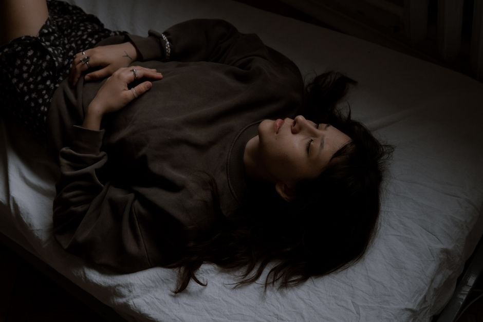 A woman lying down in a darkened room with her forearm across her eyes