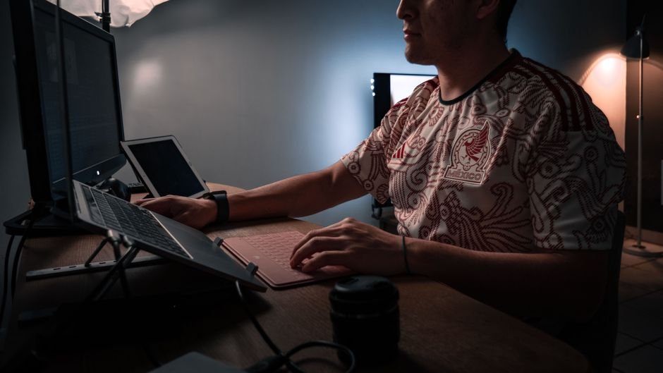A person working at a low laptop screen on a desk, seen from the side