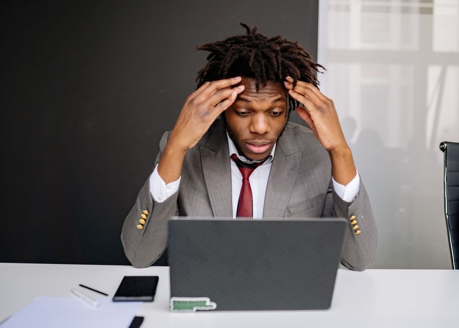 A man at a laptop with both hands pressed against his head