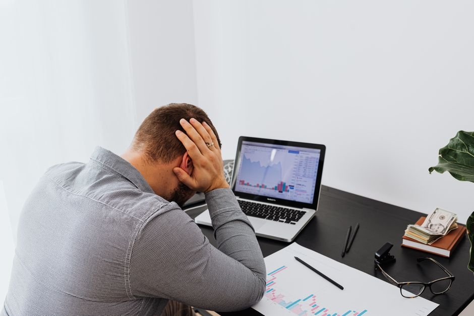 A man at a desk resting both hands on the top of his head, looking down