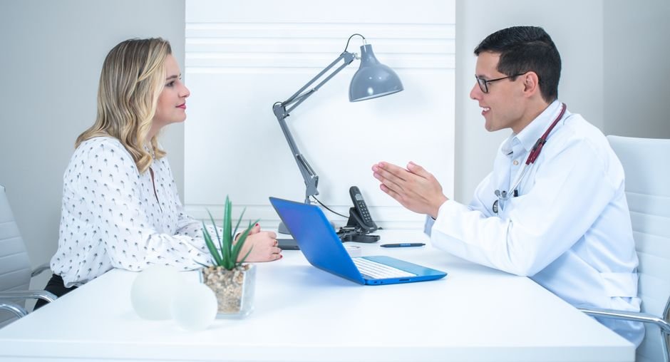 A clinician and patient in conversation across a desk in a consulting room